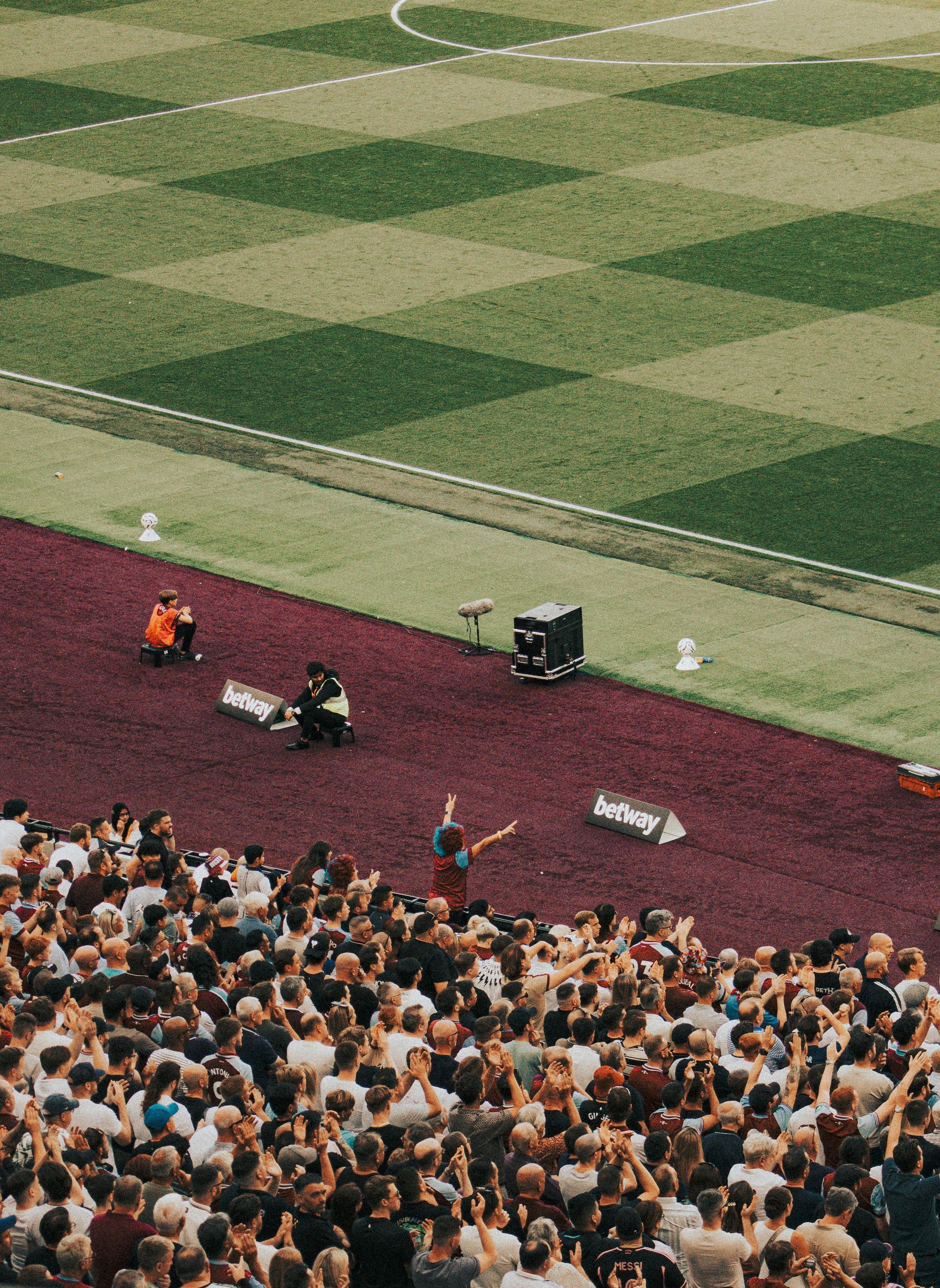 Crowd watching a live performance on a maroon field beside green patterned turf