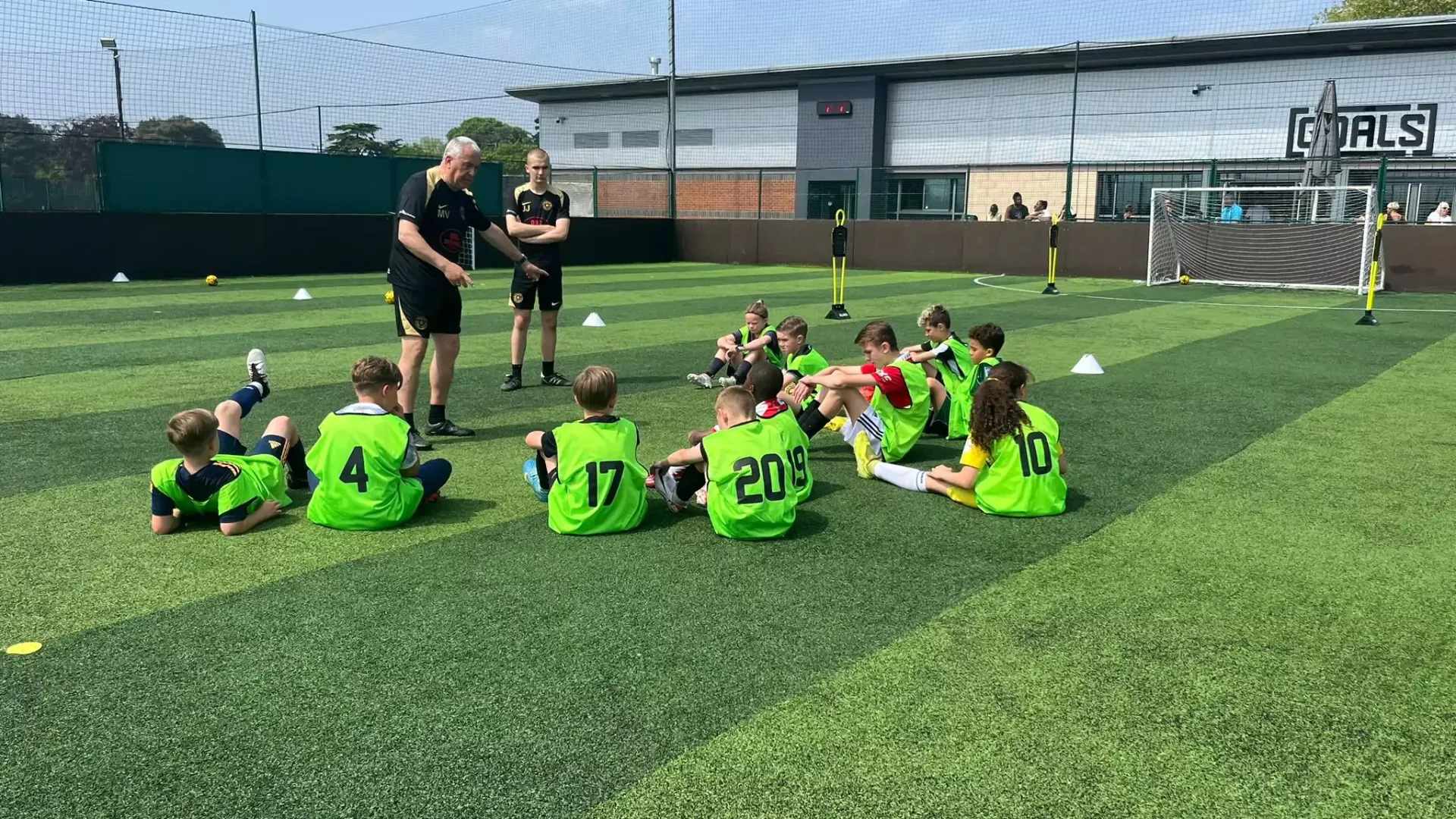 Youth soccer team in neon green jerseys listens to coaches on a sunny field