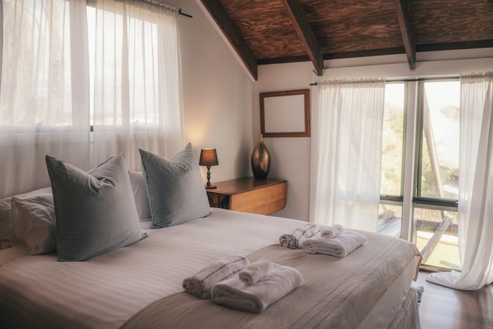 Cozy bedroom with a bed, gray pillows, folded towels, and sliding glass doors to a balcony