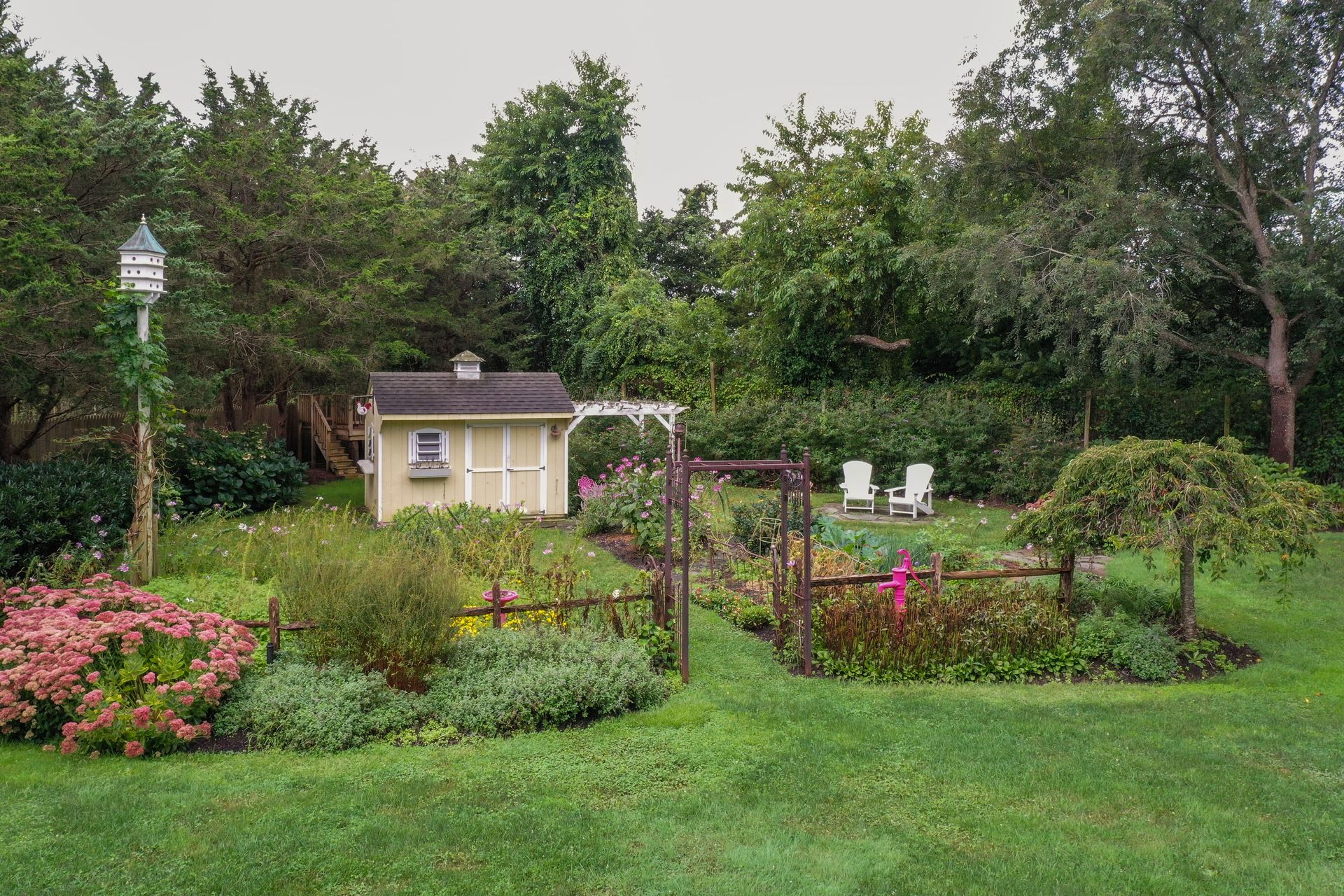 A small white shed is sitting in the middle of a garden surrounded by trees.