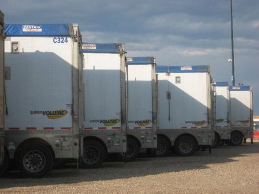 Row of white delivery trucks parked in a lot at dusk, lined up side by side.
