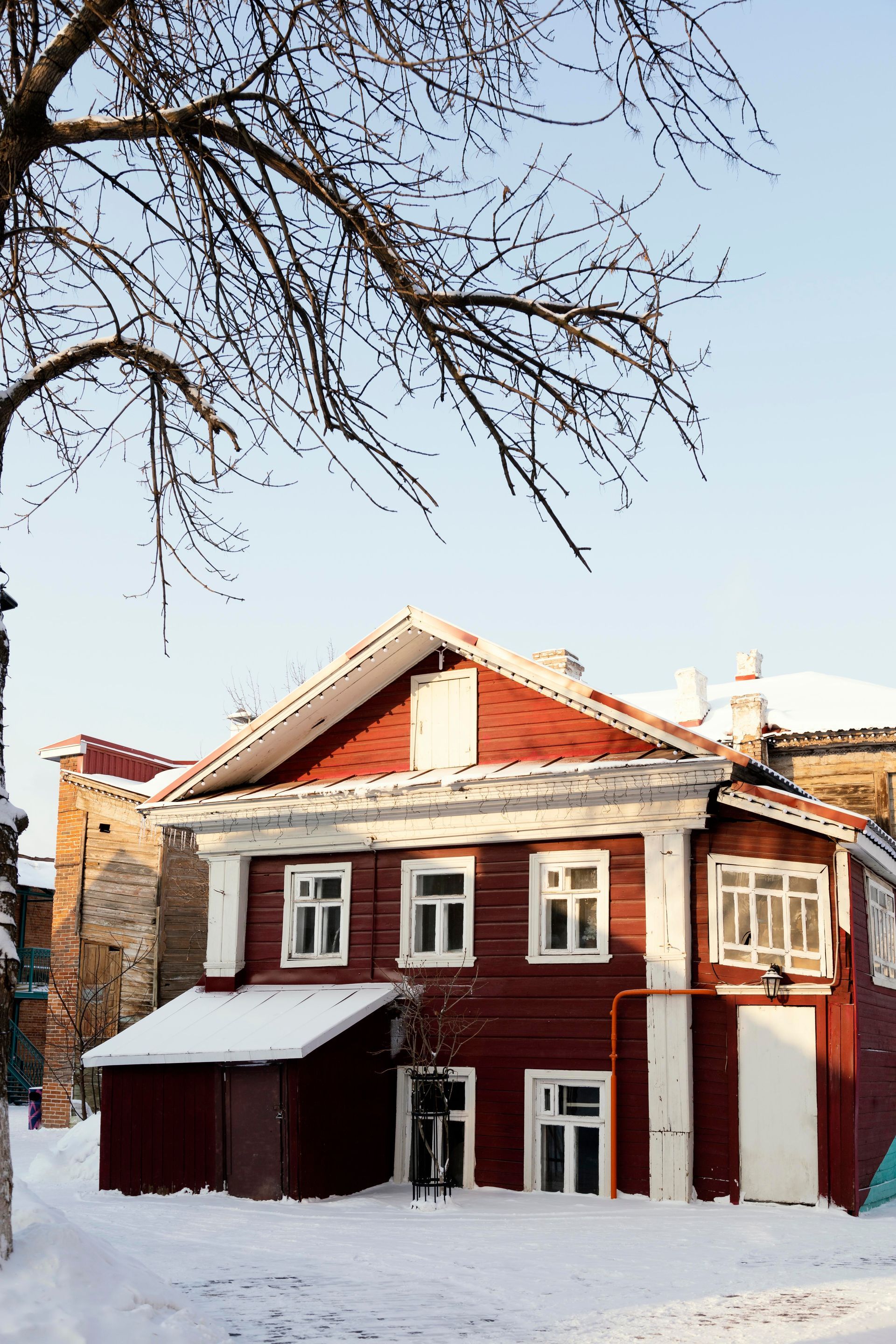 Snow-covered red house with white trim and bare tree branches overhead