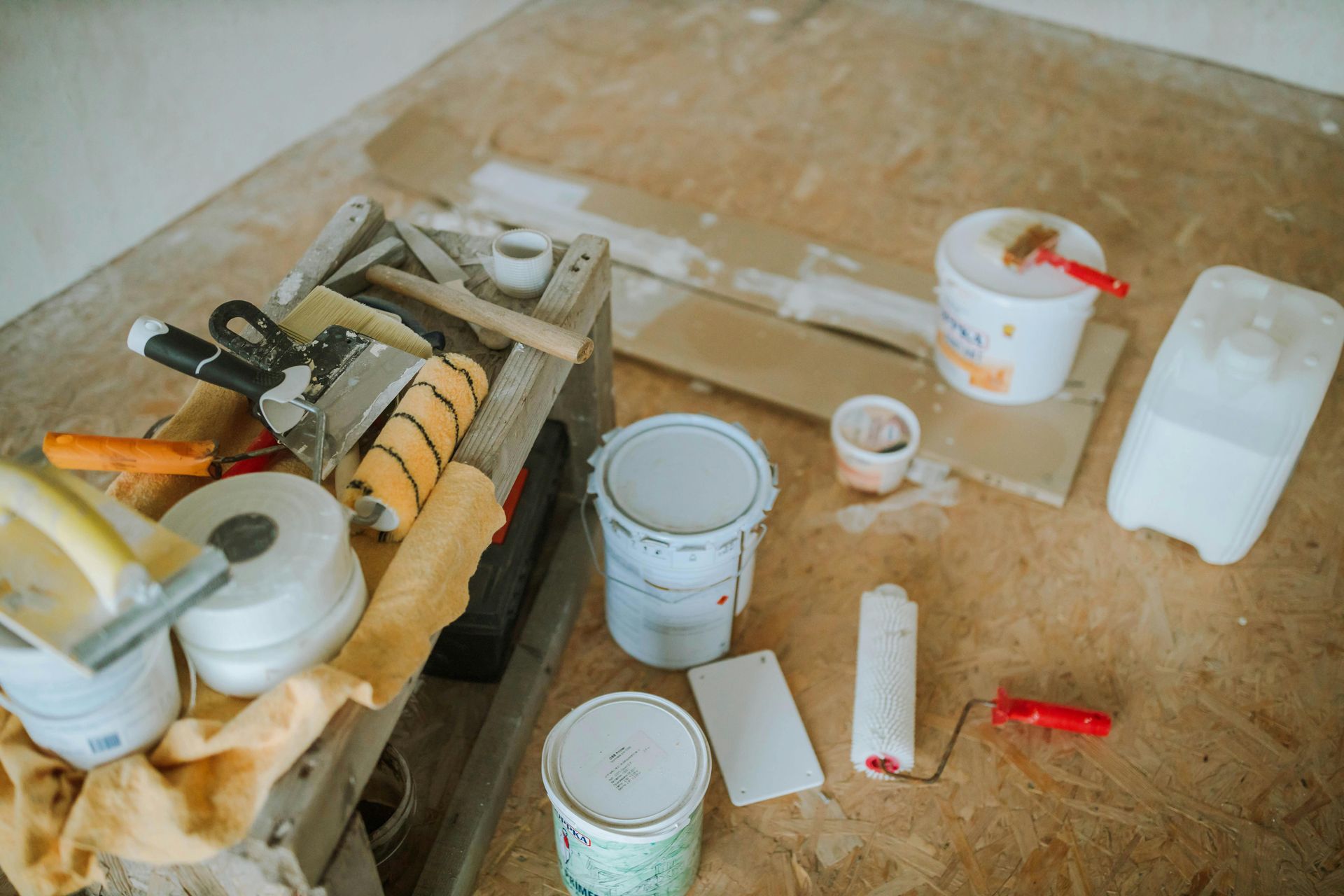 Tools and paint cans scattered on a dusty floor beside a workbench, suggesting a renovation project