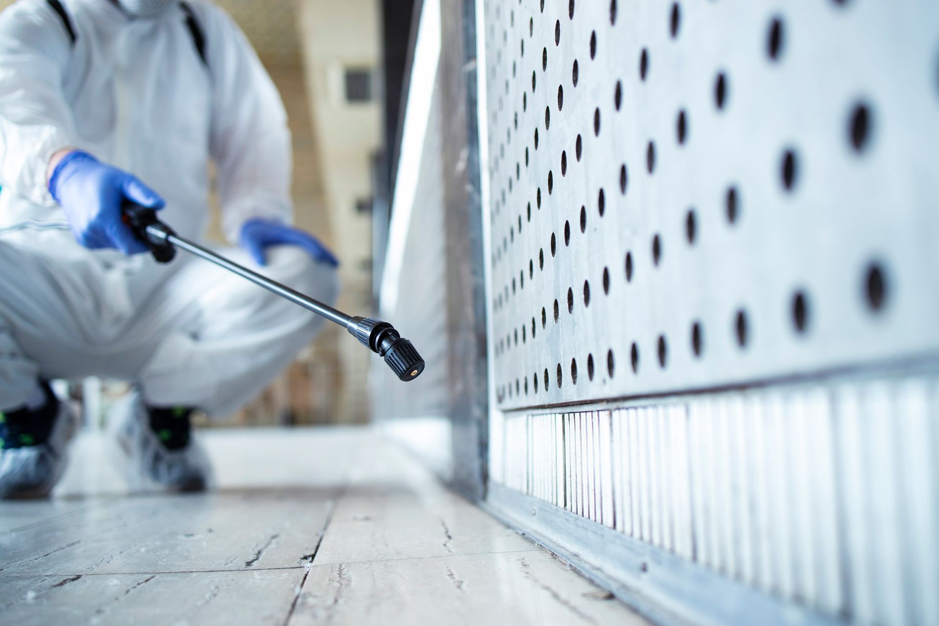 Person in protective suit spraying disinfectant along a wall with a spray wand