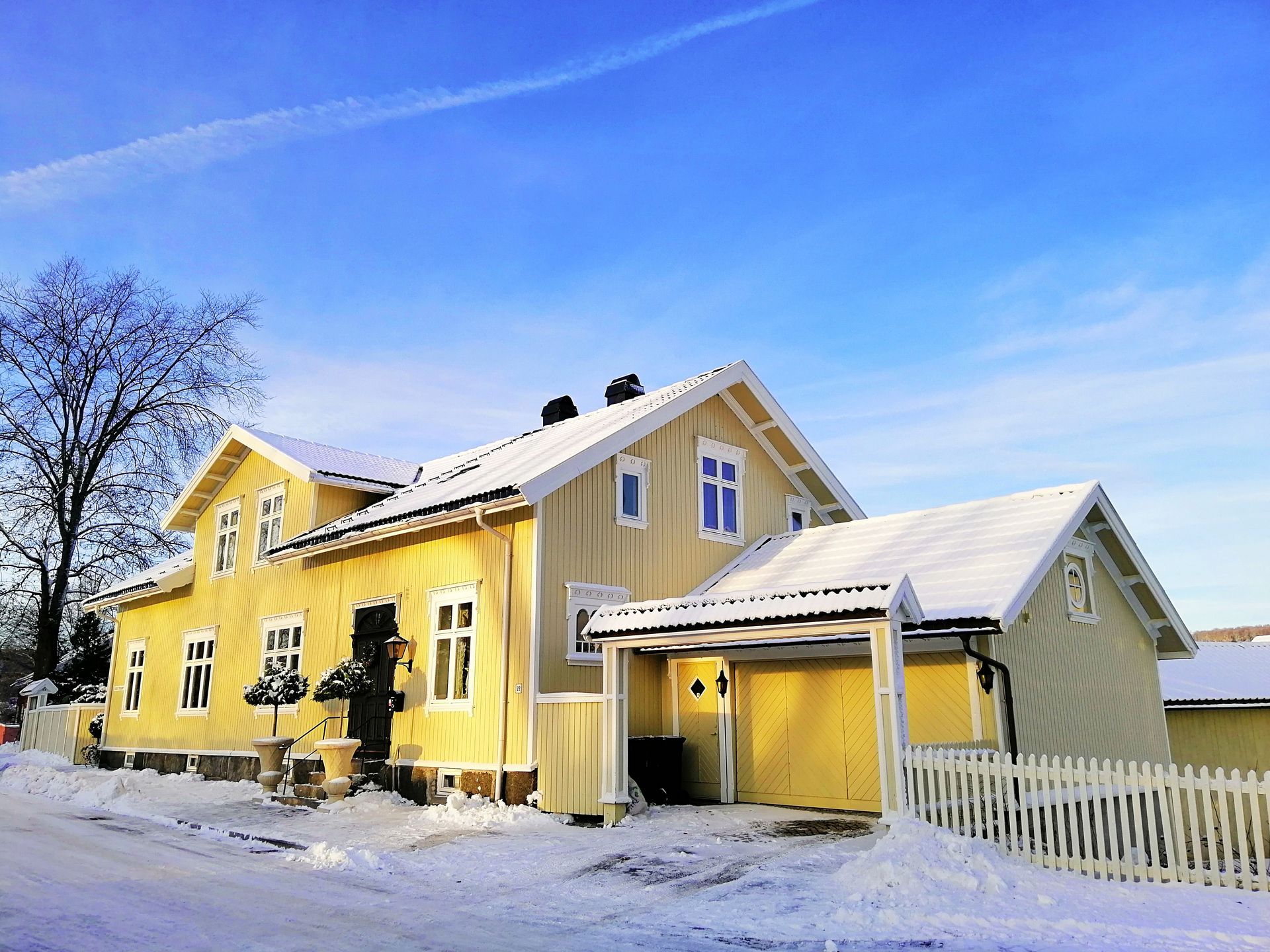 Yellow house with white trim and snow-covered yard under a blue winter sky
