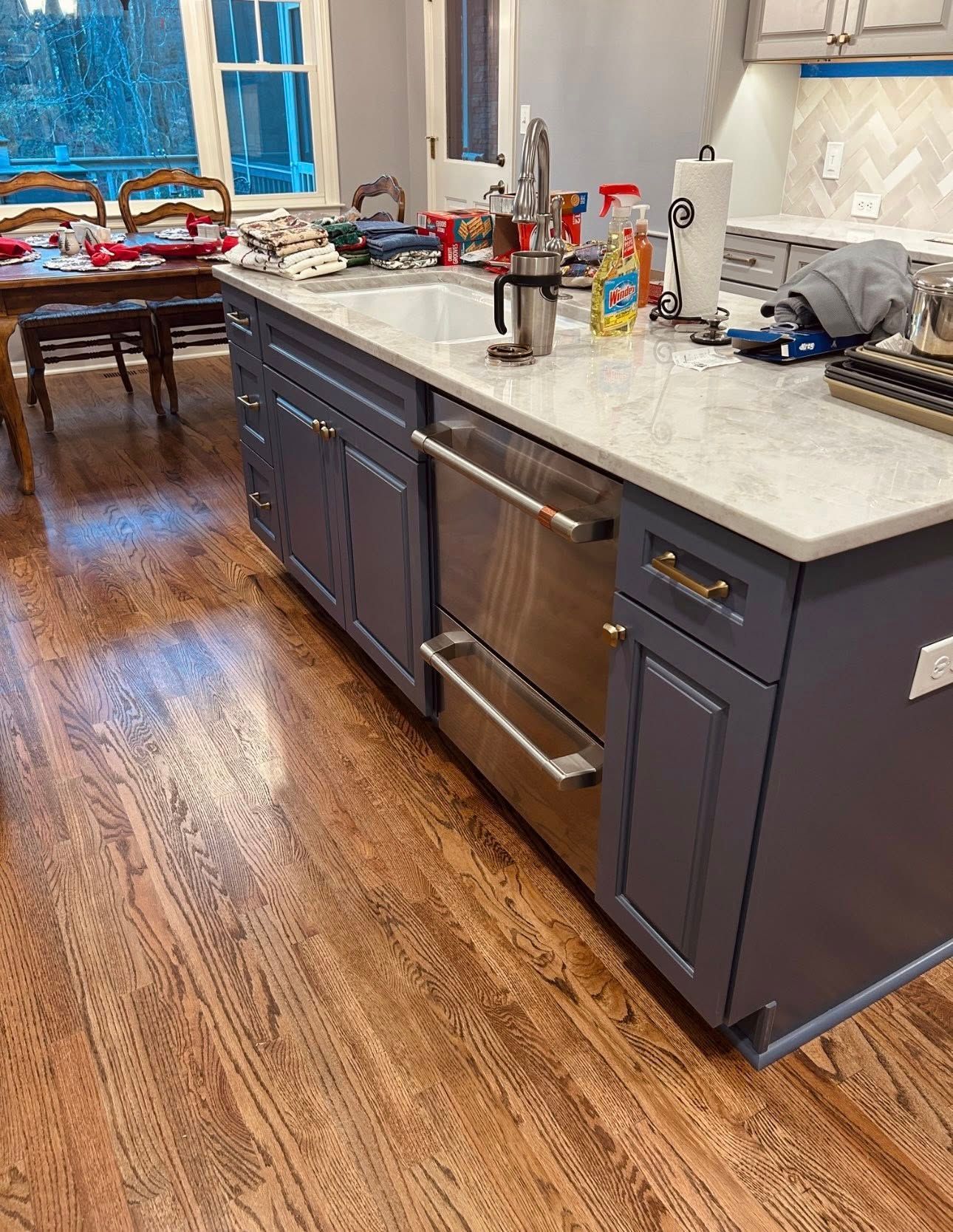 Modern kitchen with dark blue island cabinets, stainless steel oven, and a wooden dining table in the background