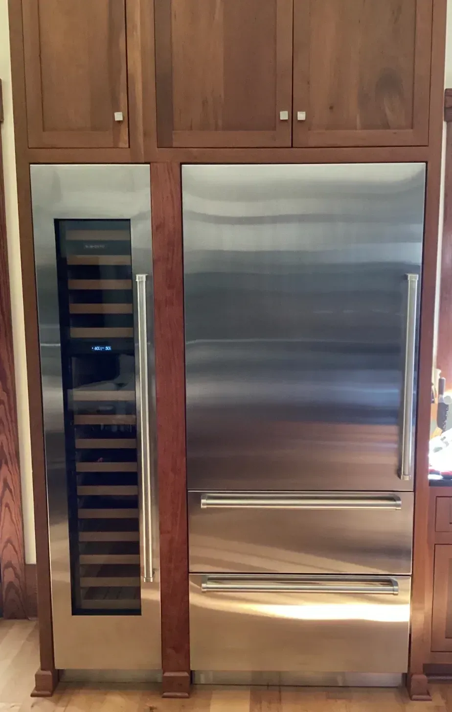 Built-in kitchen with stainless steel refrigerator and narrow wine cooler under wood cabinets