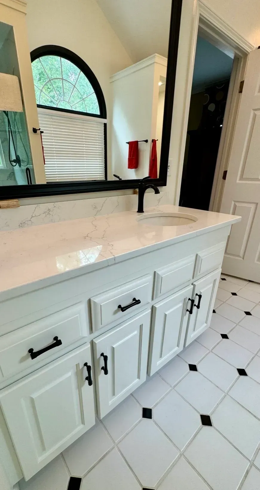 White bathroom vanity with double sink, black faucet, large mirror, and tiled floor
