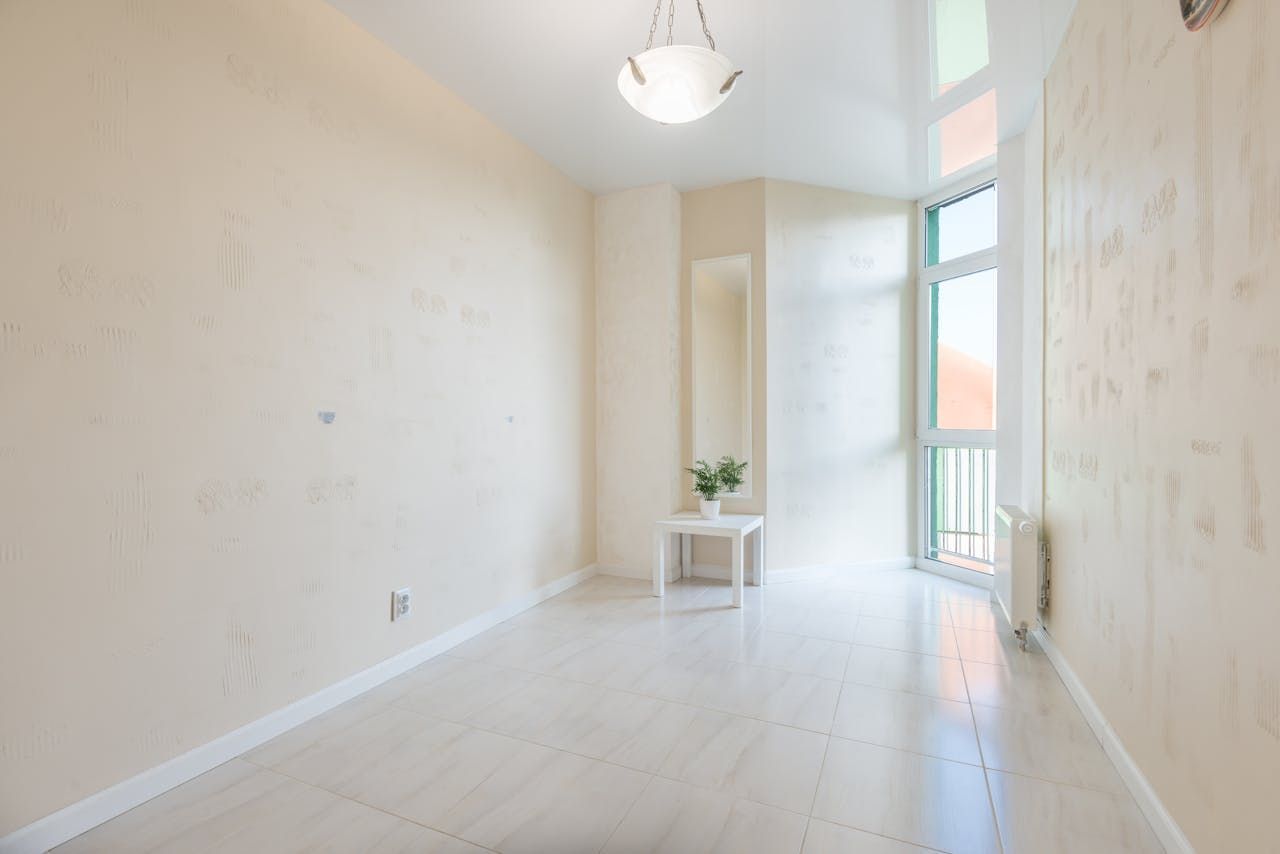 Bright empty white room with high windows, a small plant on a table, and a hanging light fixture