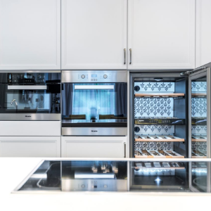 Modern built-in kitchen with white cabinets and stainless steel appliances, including an open wine fridge