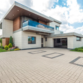Modern two-story house with balcony, large paved driveway, and landscaped front yard