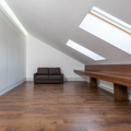 Bright attic room with wood floors, skylights, a brown sofa, and a wooden table.