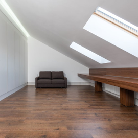 Empty room with dark wood floors and a small staircase leading to an open doorway Minimal attic room with sloped skylights, wood floor, gray sofa, and long wooden table