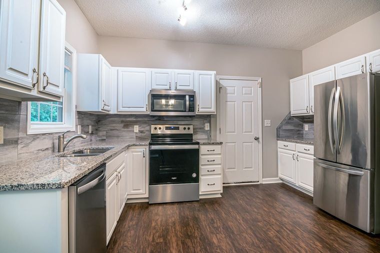 Bright modern kitchen with white cabinets, stainless steel appliances, granite counters, and dark wood flooring Bright modern kitchen with white cabinets, stainless steel appliances, granite counters, and dark wood flooring