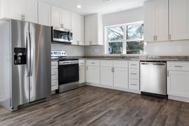 Bright modern kitchen with stainless steel appliances, white cabinets, and wood flooring