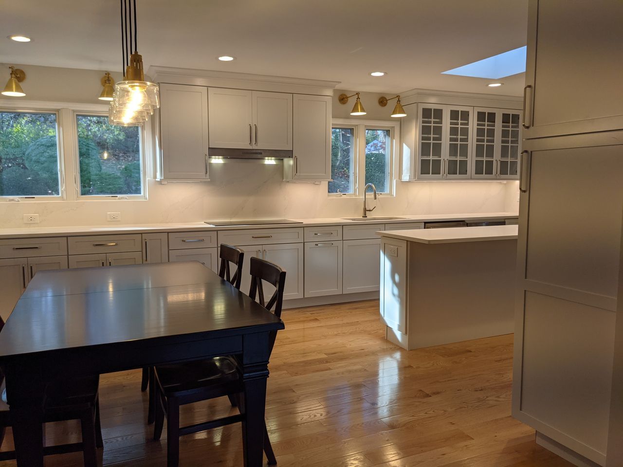 Bright white kitchen with island, dark dining table, hardwood floors, and large windows Bright white kitchen with island, dark dining table, hardwood floors, and large windows