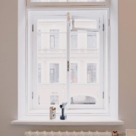 Modern white kitchen with gray marble backsplash, stainless steel fridge, and gas stove White window with city buildings outside and a small windowsill with a bottle and dark figurine