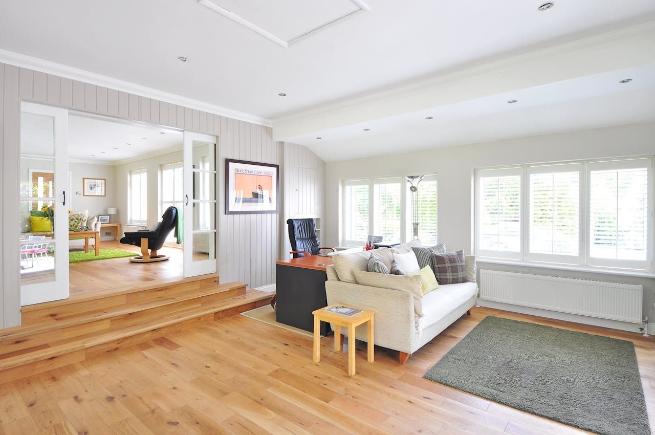 Bright, open living room with white sofa, wood floors, large windows, and a raised dining area.