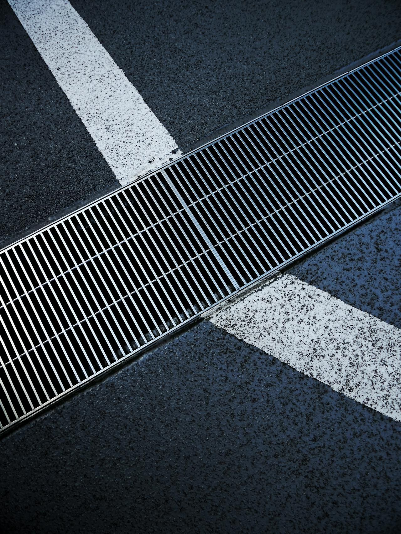 Diagonal metal drainage grate crossing white road markings on dark asphalt