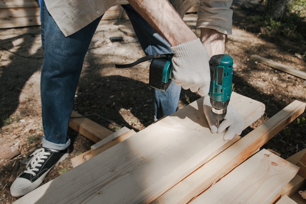 Person using a teal drill to screw a white board on outdoor wooden planks
