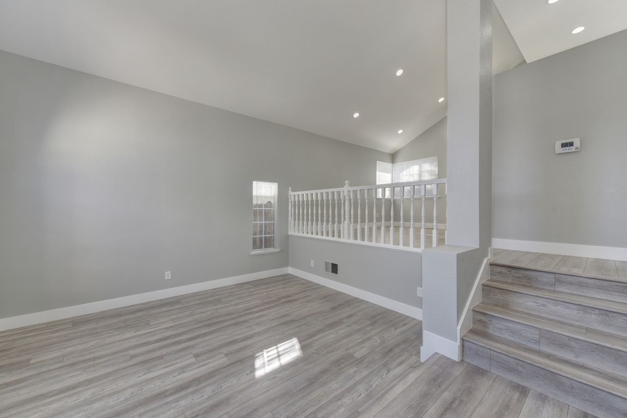 Empty modern living room with gray walls, carpet, stairway, and white railing Empty modern living room with gray walls, carpet, stairway, and white railing