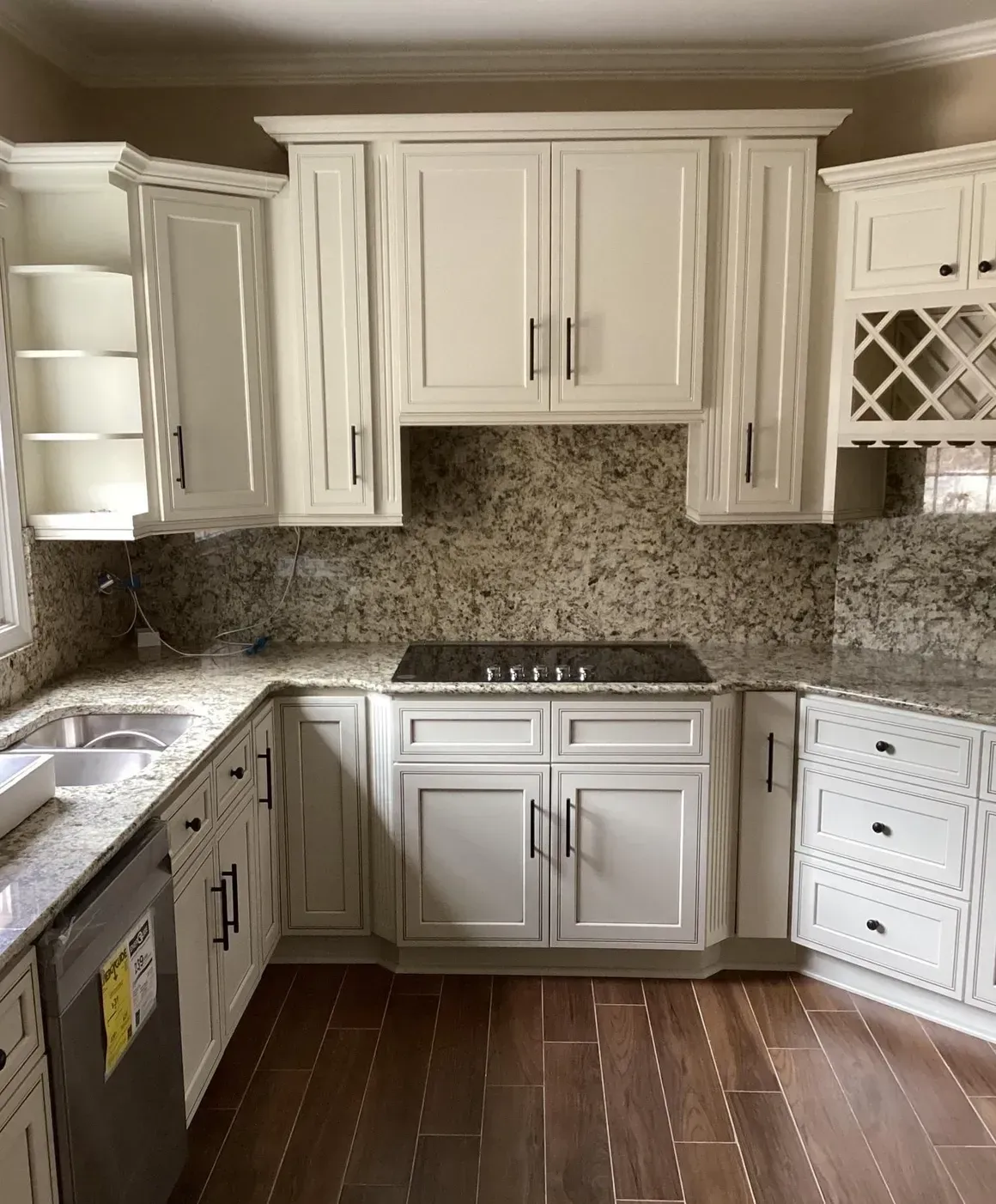 Bright kitchen with white cabinets, speckled stone backsplash, dark wood floor, and stainless stove.