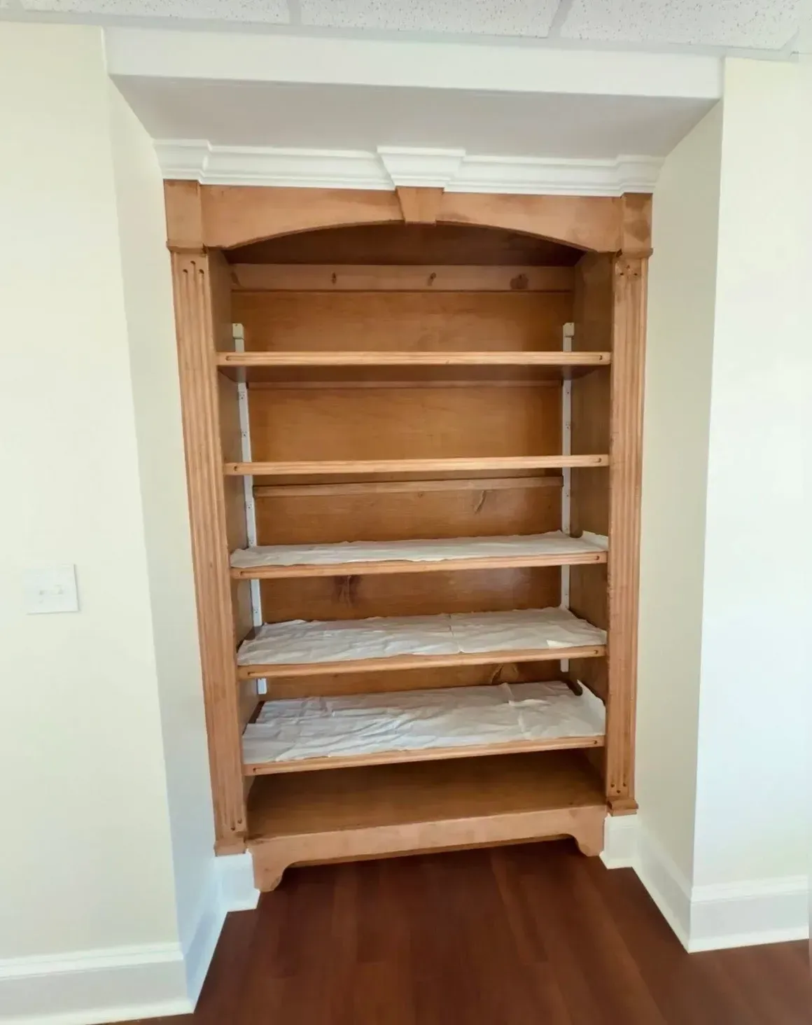Empty recessed wooden shelving unit in a white wall niche above a hardwood floor