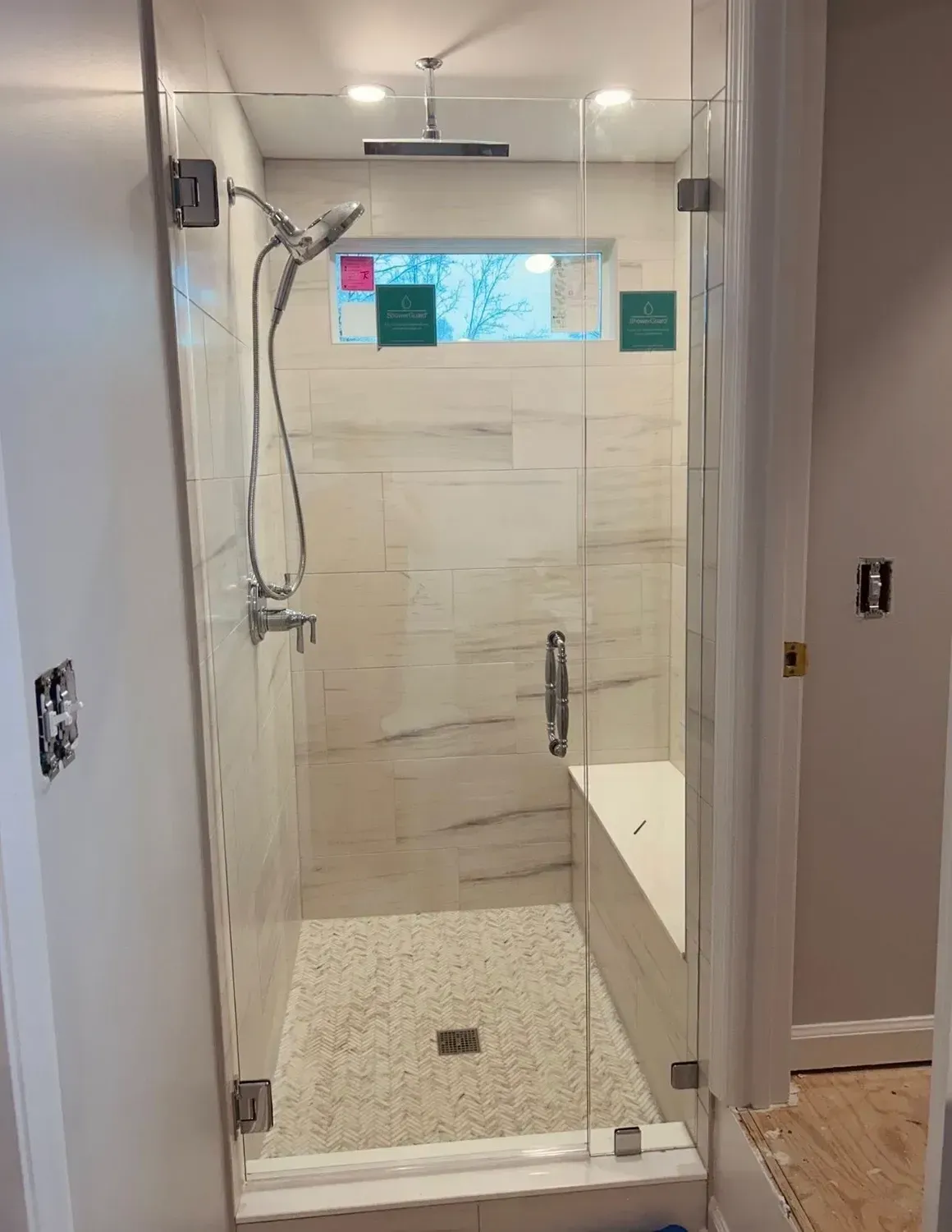 Modern glass shower enclosure with beige tile, pebble floor, and built-in bench in a bathroom