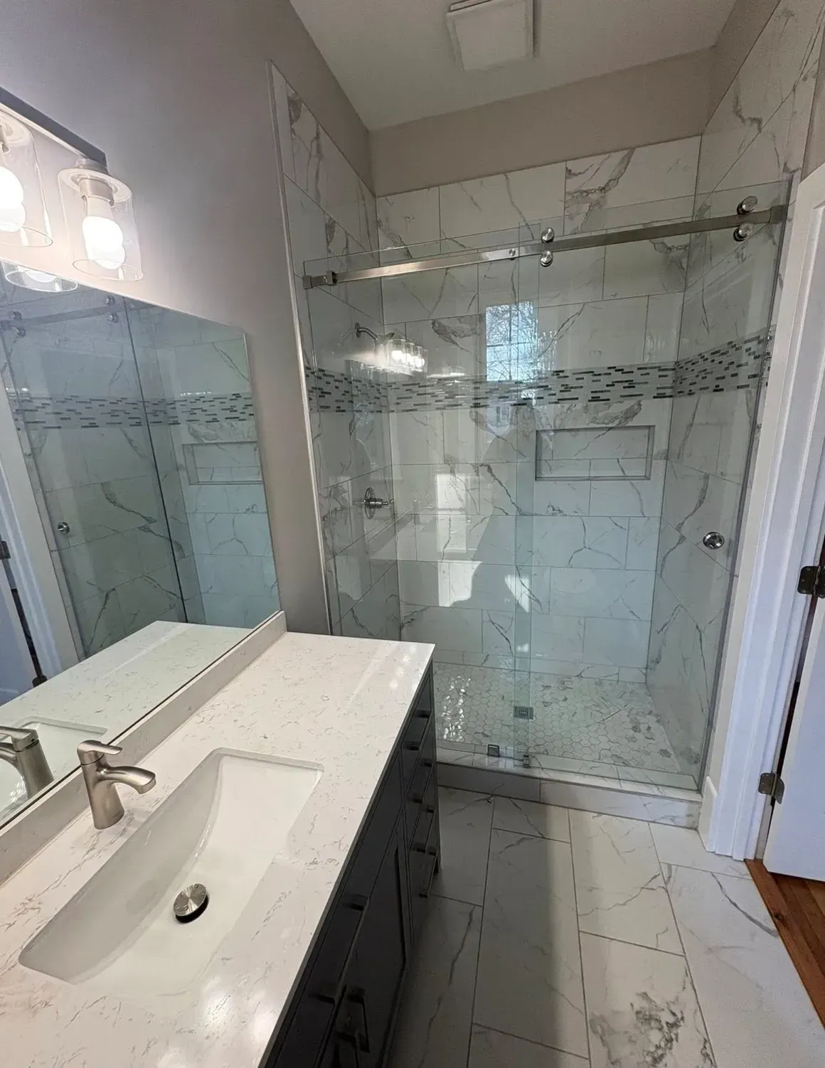 Modern bathroom with double sinks, glass shower enclosure, and white tile floor and walls