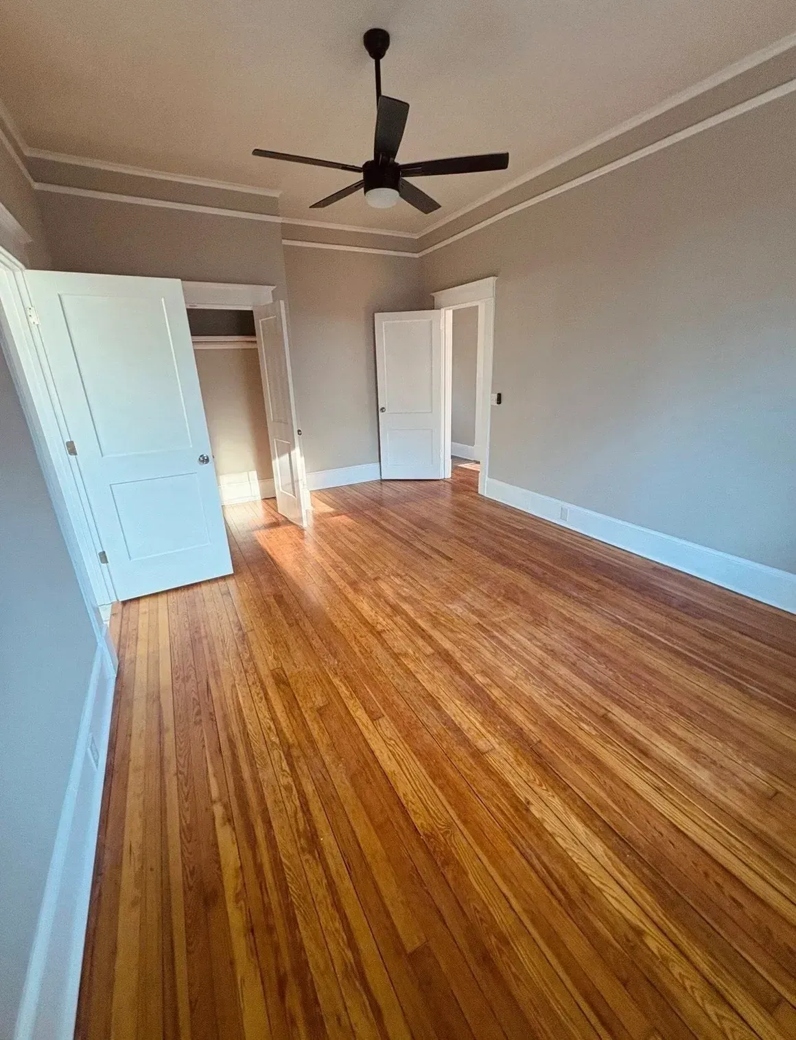 Empty bedroom with hardwood floors, white walls, open doors, and a ceiling fan