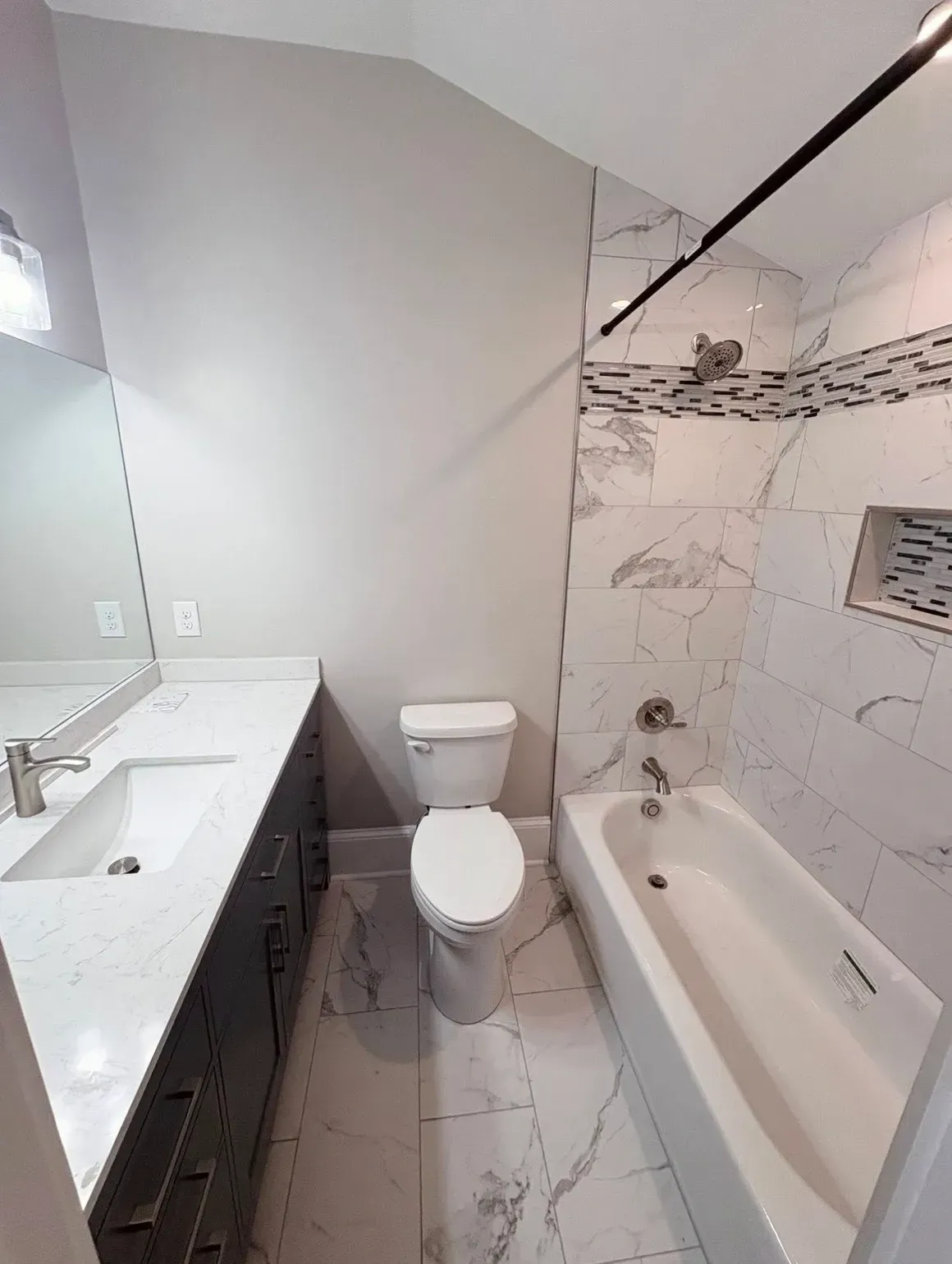 Small bathroom with white vanity, toilet, and marble-tiled bathtub/shower.