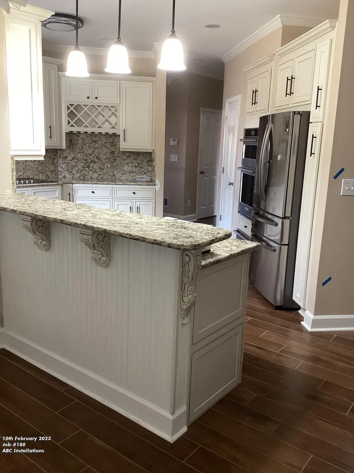 Bright kitchen with granite island, white cabinets, pendant lights, and stainless steel refrigerator.