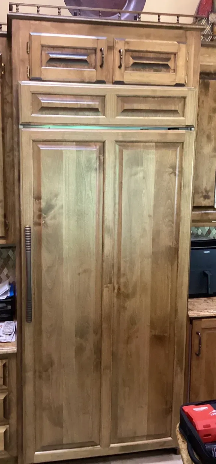 Tall wooden cabinet with two doors and small top drawers, in a workshop or storage area