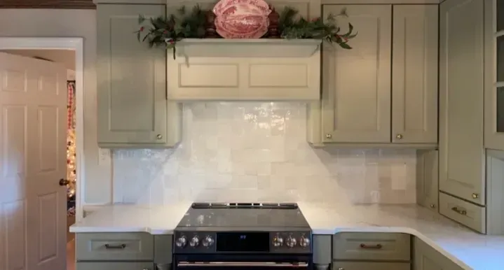 Bright kitchen with white cabinets, marble backsplash, and black stove beneath a shelf with pink flowers
