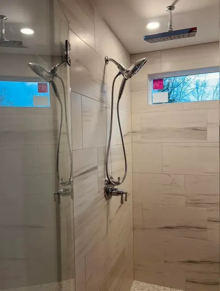 Modern bathroom shower with glass enclosure, tiled walls, and chrome fixtures beneath two small windows