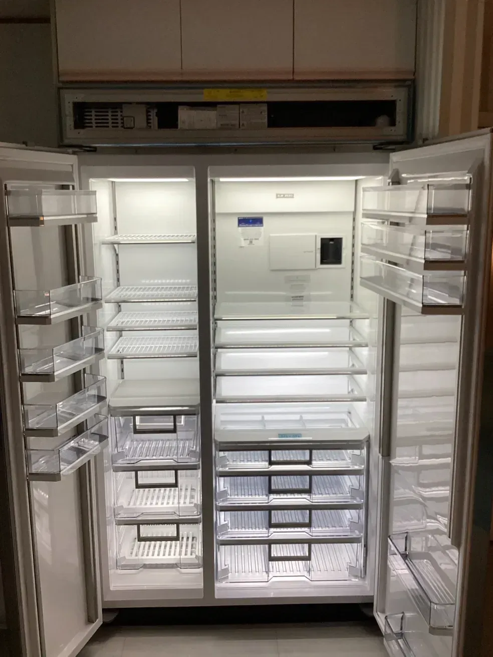 Open refrigerator filled with stacks of labeled plastic storage containers on shelves and in the doors