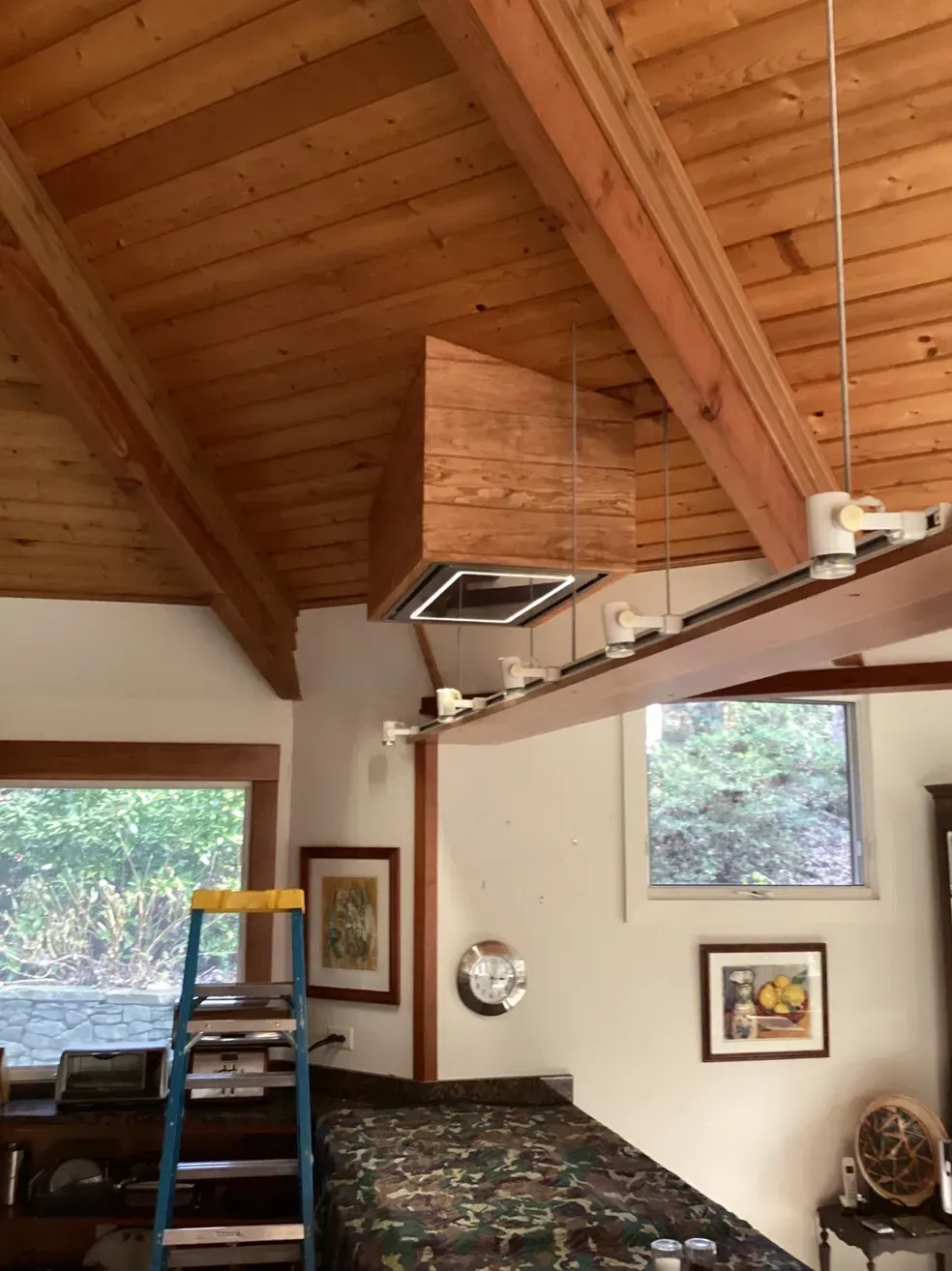 Wood-paneled vaulted ceiling over a cozy bedroom with a bed and large windows overlooking trees.