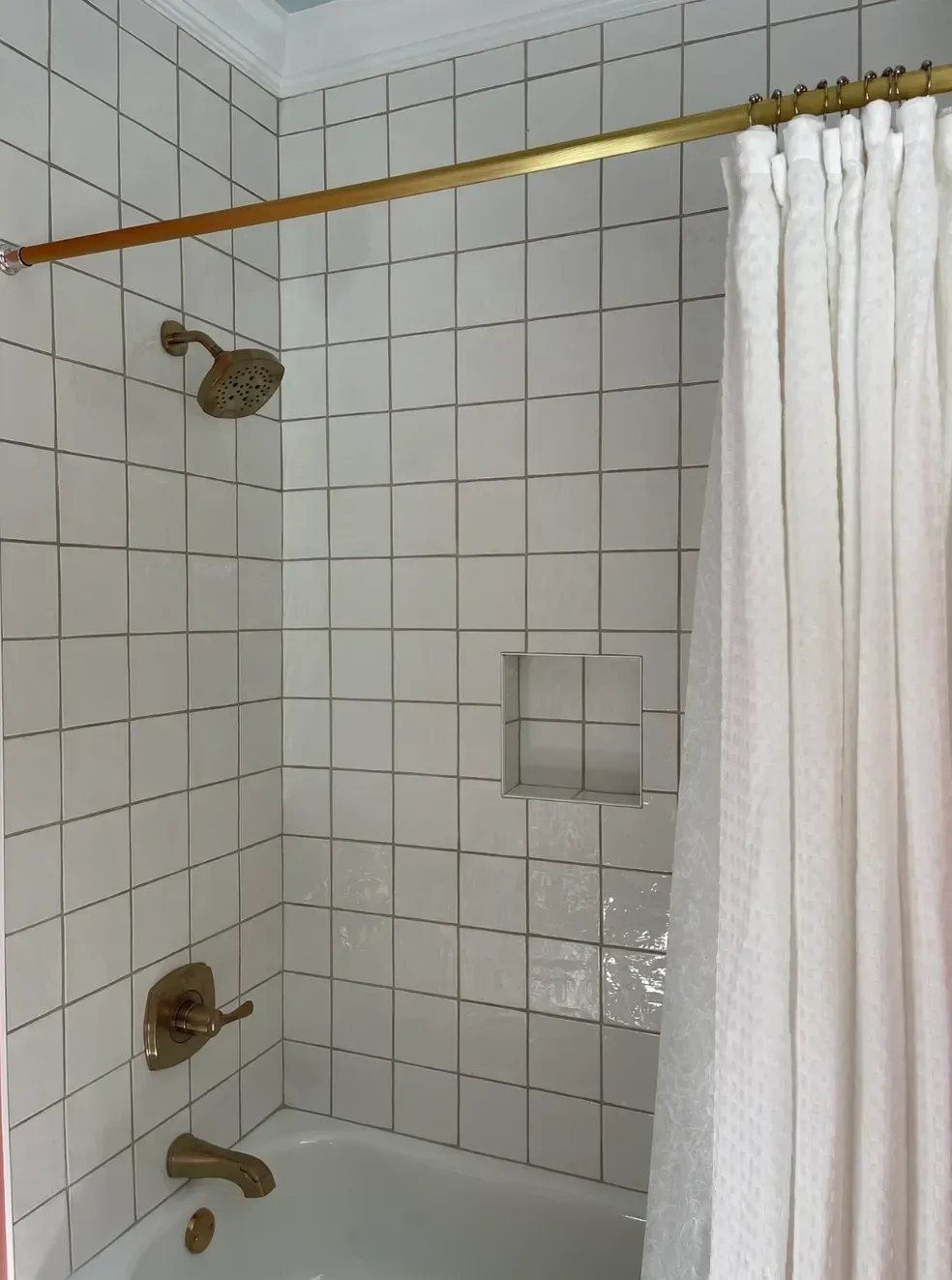 White tiled shower with curtain, grab bar, and faucet fixtures