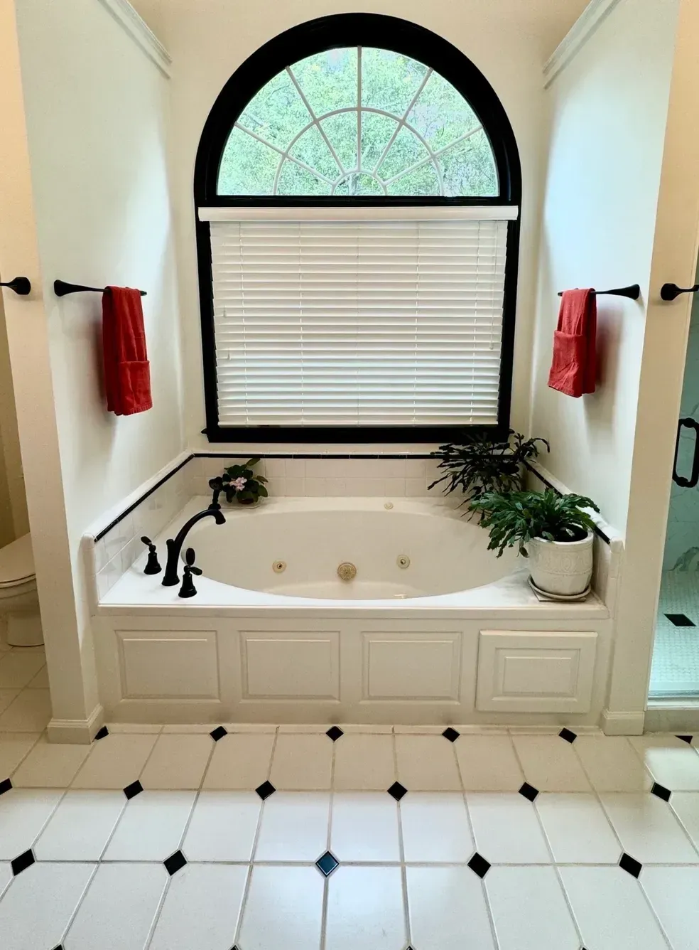 Bright bathroom with a white soaking tub beneath an arched window and tiled floor