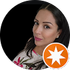 Close-up portrait of a woman with dark hair and pink lipstick, wearing a white top with an orange star badge