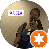 Person taking a mirror selfie, wearing a blue tank top, with a UCLA sticker and orange star icon overlay.