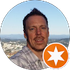 Headshot of a smiling man outdoors with a city skyline in the background and an orange star badge overlay