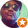 Close-up selfie of a person wearing sunglasses, with a small orange star badge in the corner