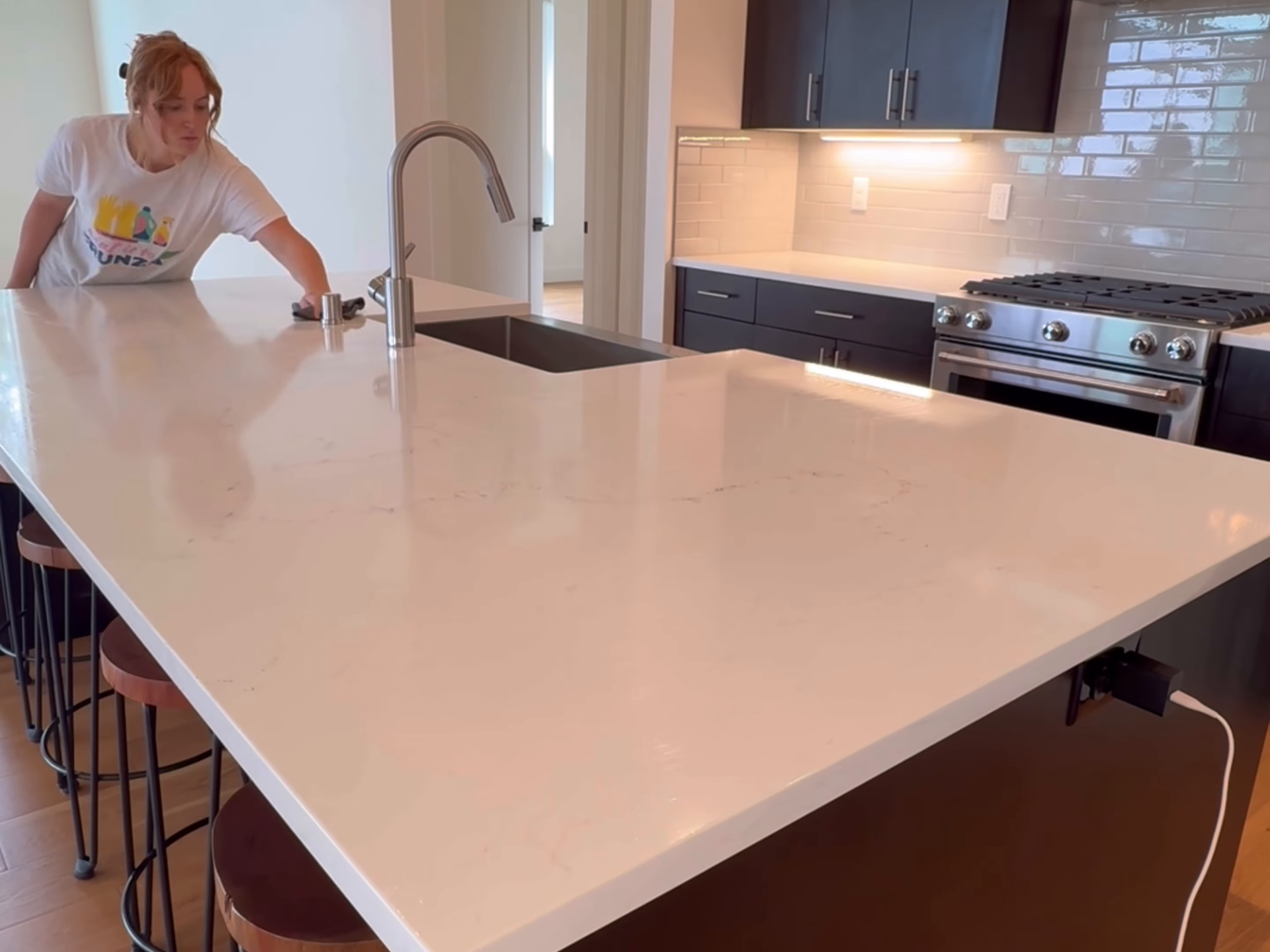 Modern kitchen with a large white island; a person stands at the counter near the sink.