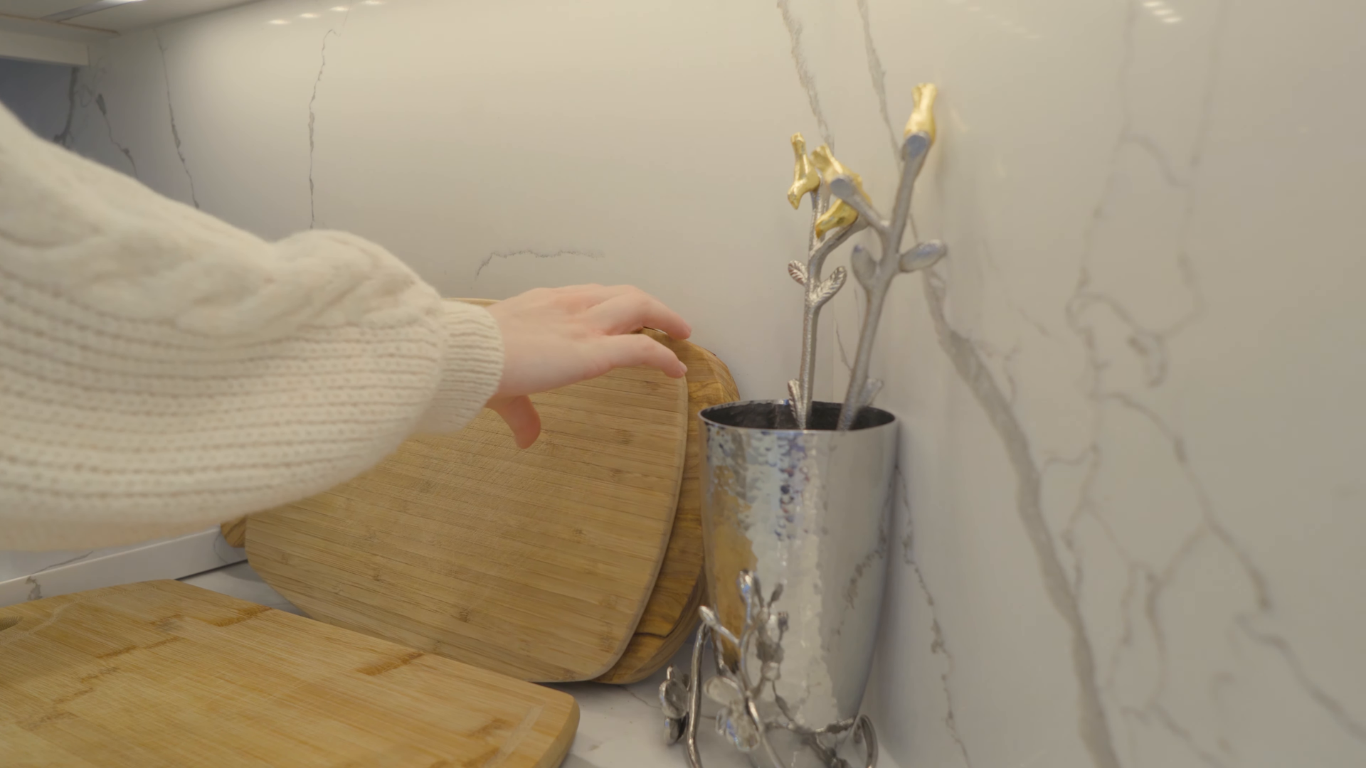 Hand placing a wicker basket beside a silver vase on a marble countertop