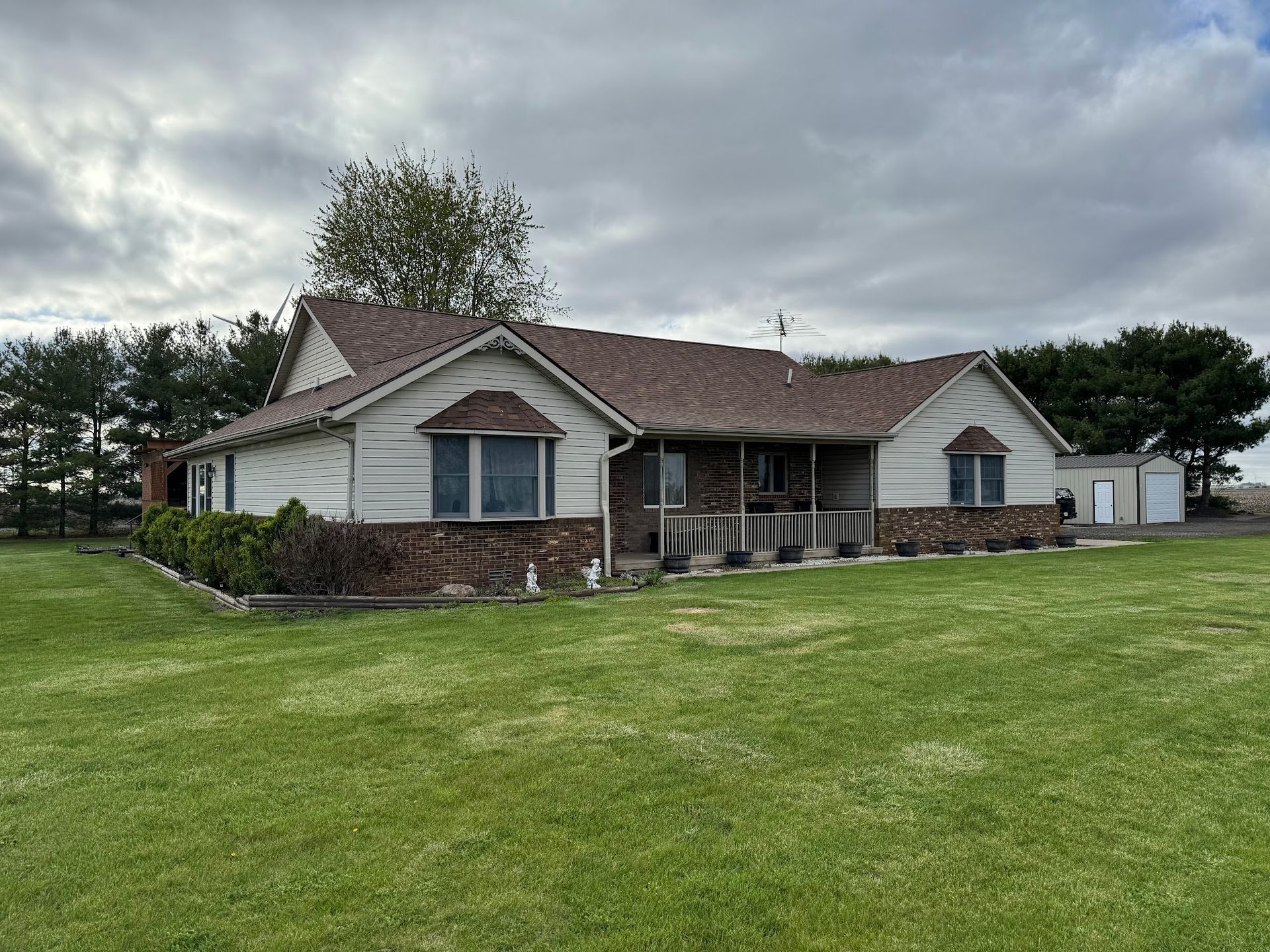 Ranch-style house with brick and siding, brown roof, large green yard, cloudy sky.
