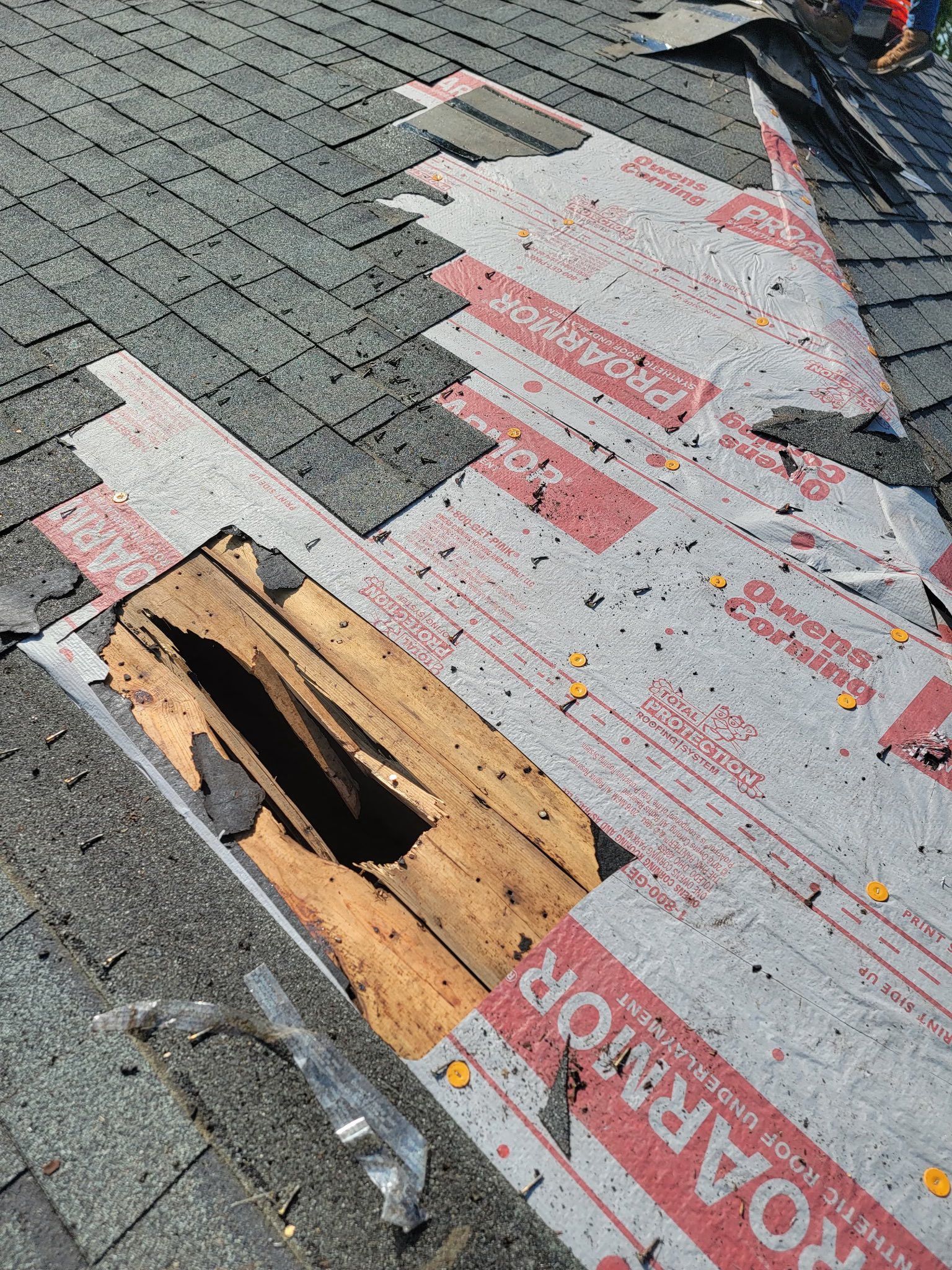 Roof repair showing exposed underlayment and damaged wood. Grey shingles partially removed.