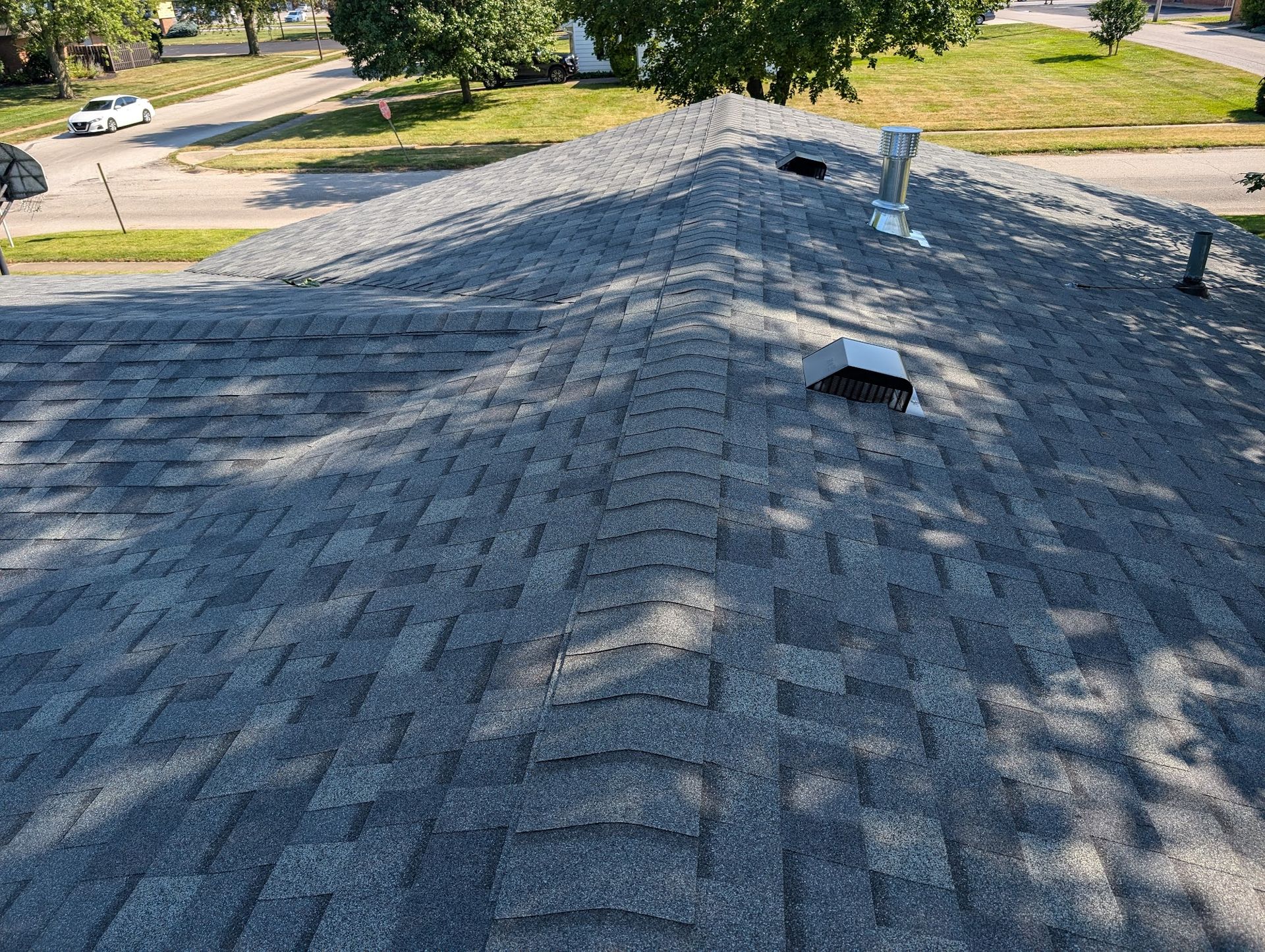 Gray asphalt shingle roof with vents, viewed from above, in a sunny outdoor setting.