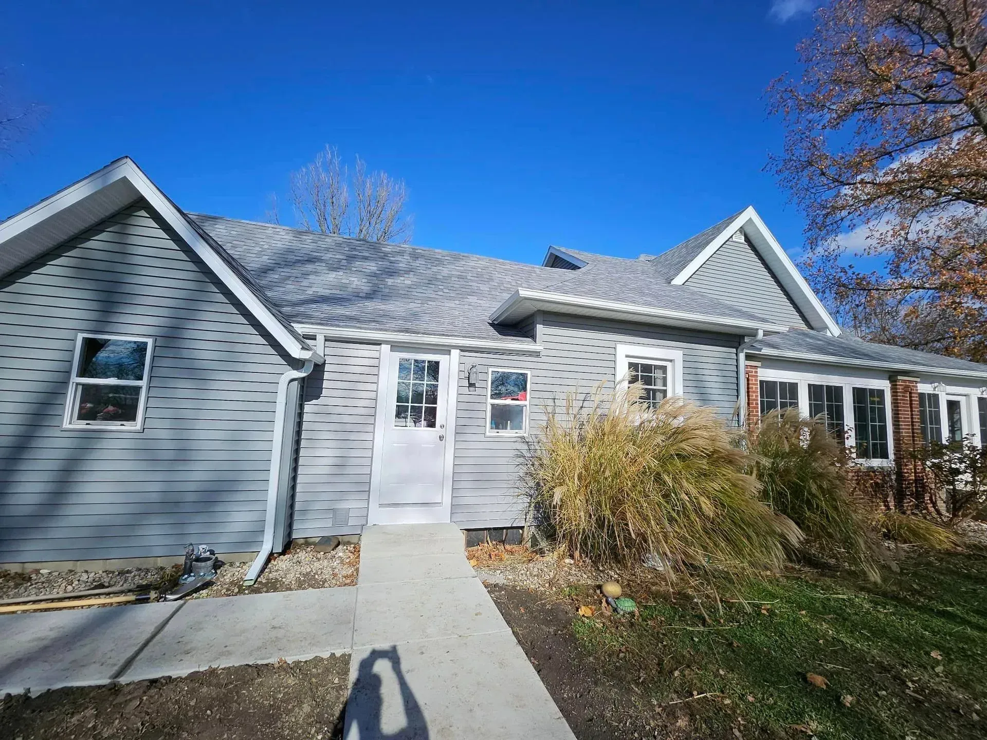 Gray house with a light gray door, white trim, and a concrete walkway on a sunny day.