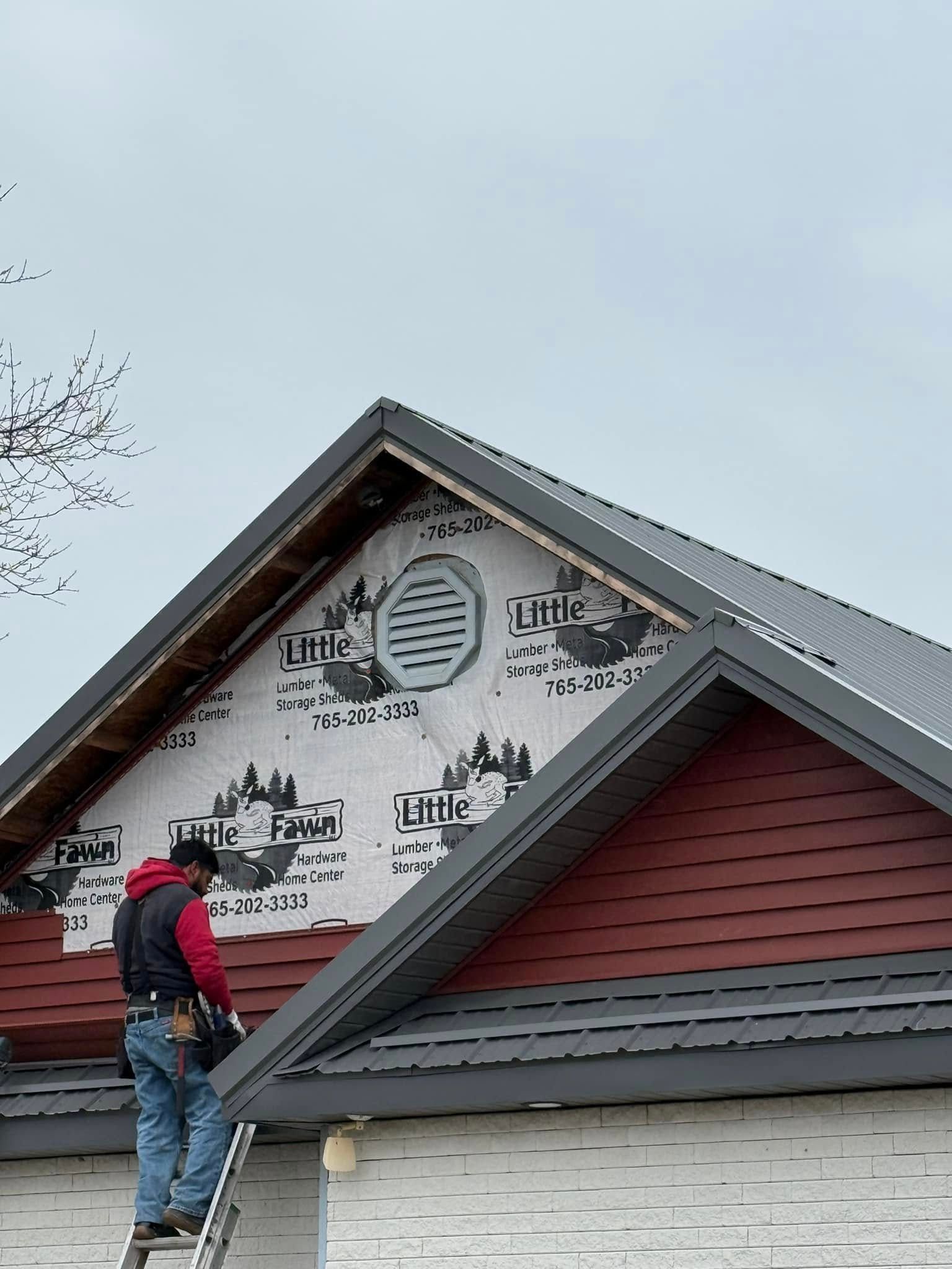 Construction worker on a ladder installing roof siding. Red siding, gray trim, an